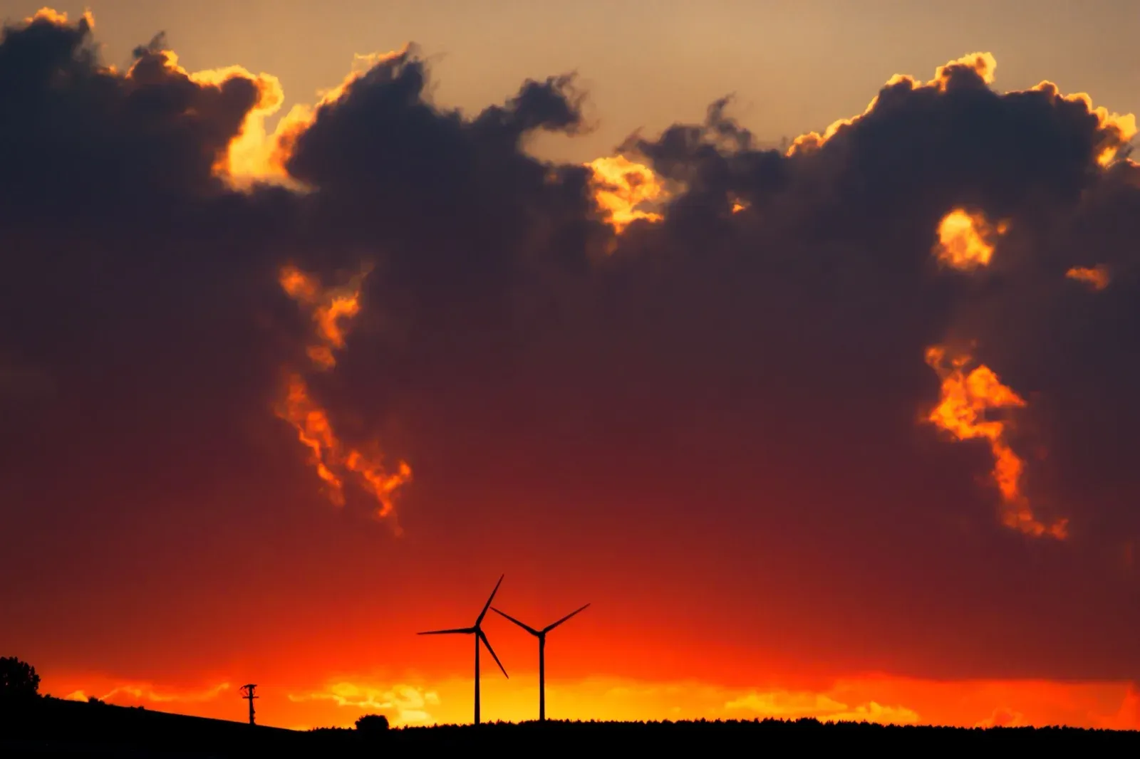 Two wind turbines silhouetted against a burning sunset
